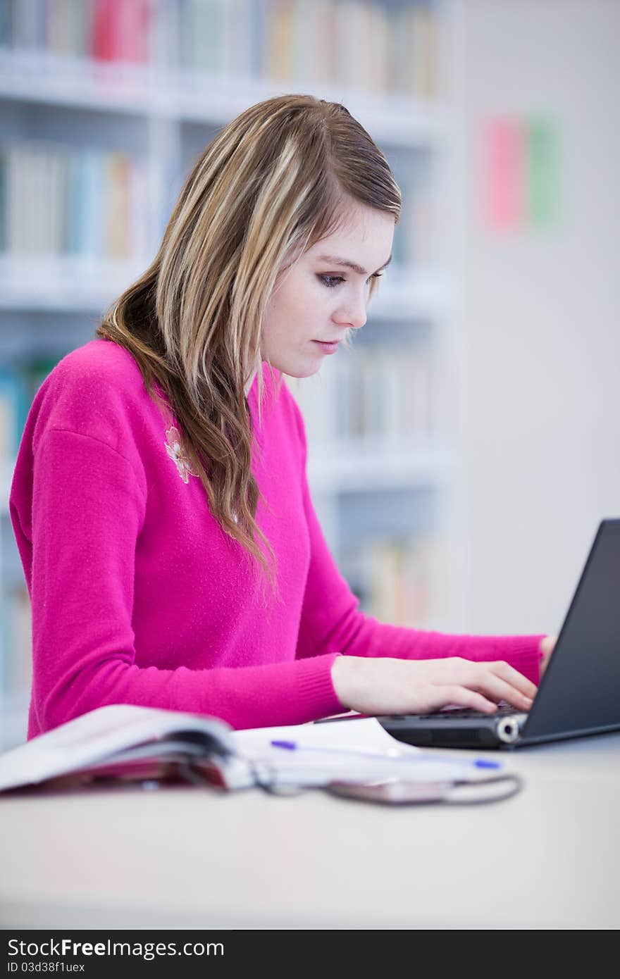 In the library - pretty, female student with laptop and books working in a high school library (color toned image)