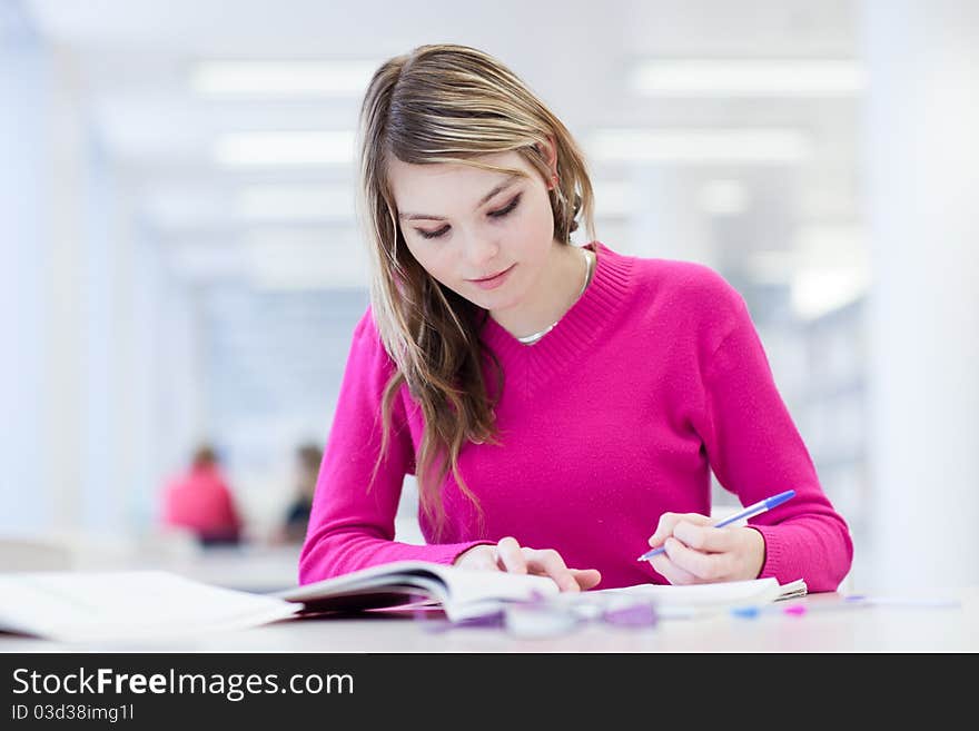 In the library - pretty, female student with laptop and books working in a high school library (color toned image)