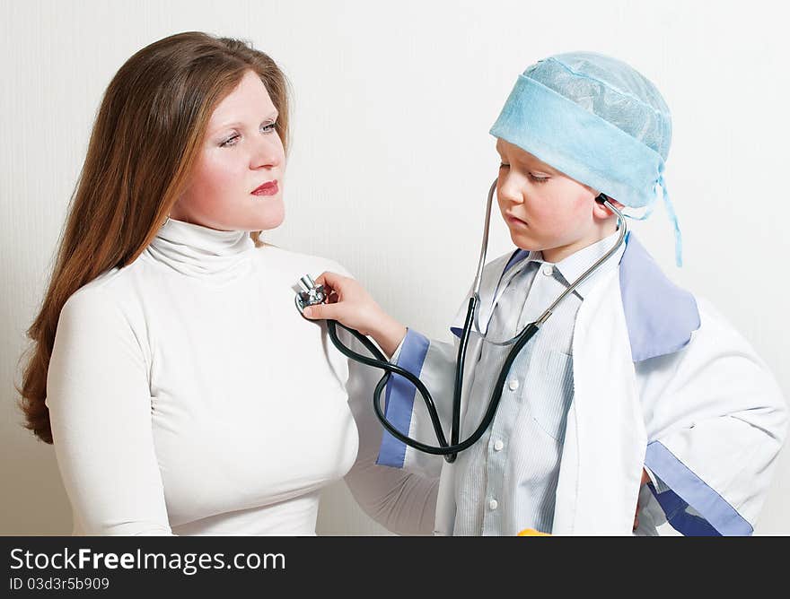 The boy plays the doctor. Listens a stethoscope to the mum