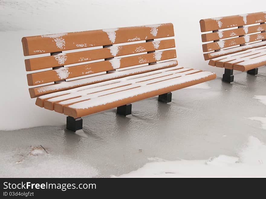 This is two orange bench in a park in a snow storm. This is two orange bench in a park in a snow storm.