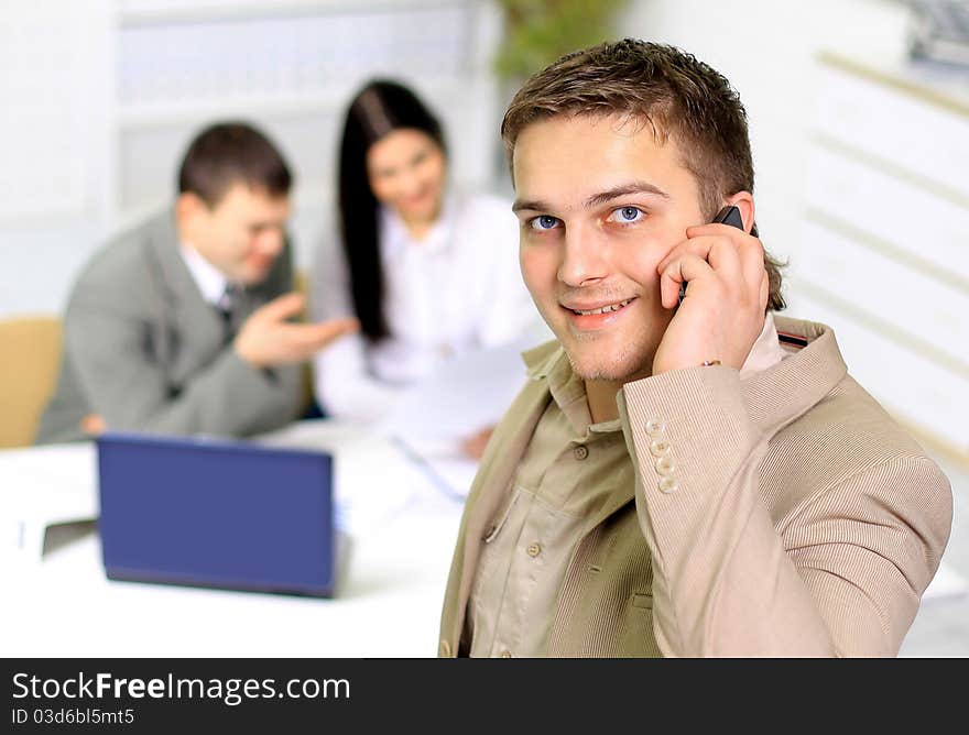 Young smiling businessman calling on phone at office