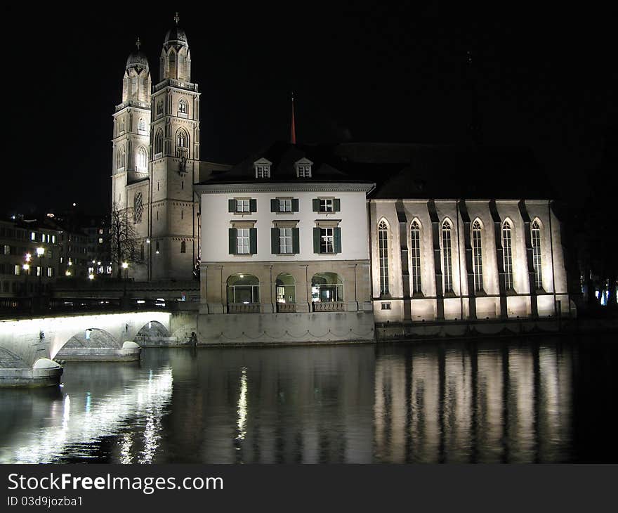 Night photo of Zurich cathedrale on the lake. Many lights creating great reflections of cathedrale and bridge.