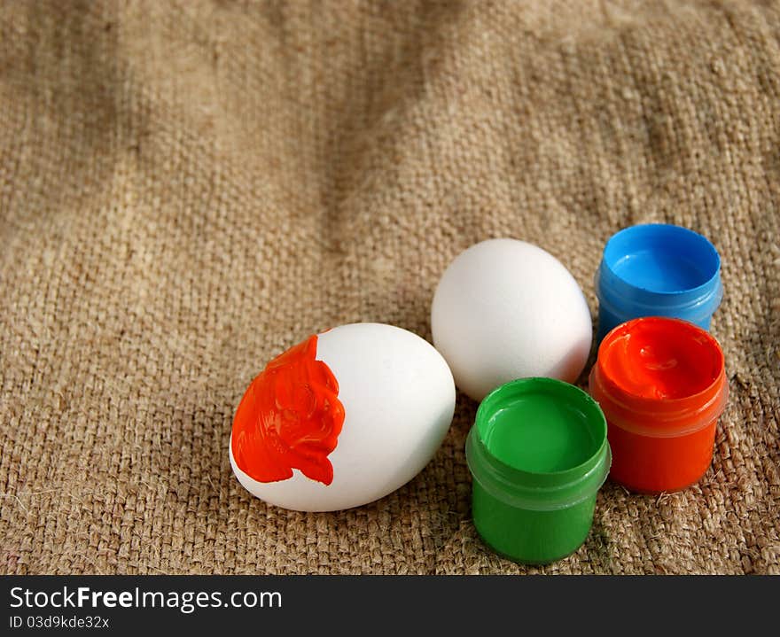 Easter eggs and jars with a bright paint on a rough canvas background