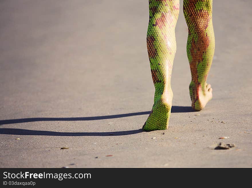 Human legs with snake skin walking along the beach. Human legs with snake skin walking along the beach.