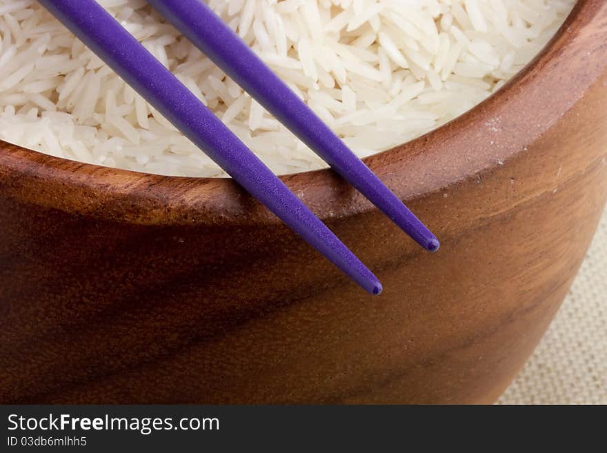 Close-up of white rice in a brown plate and purple chopsticks.