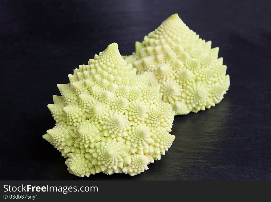 A pair of pale green baby cavolo romanesco on a slate surface