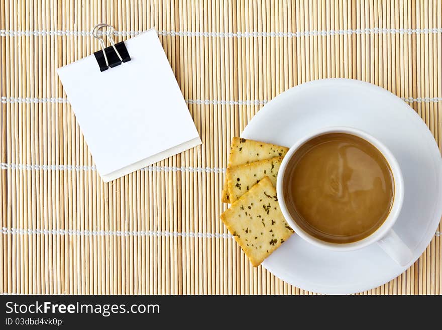 White cup of hot coffee and white sketch book on a mat