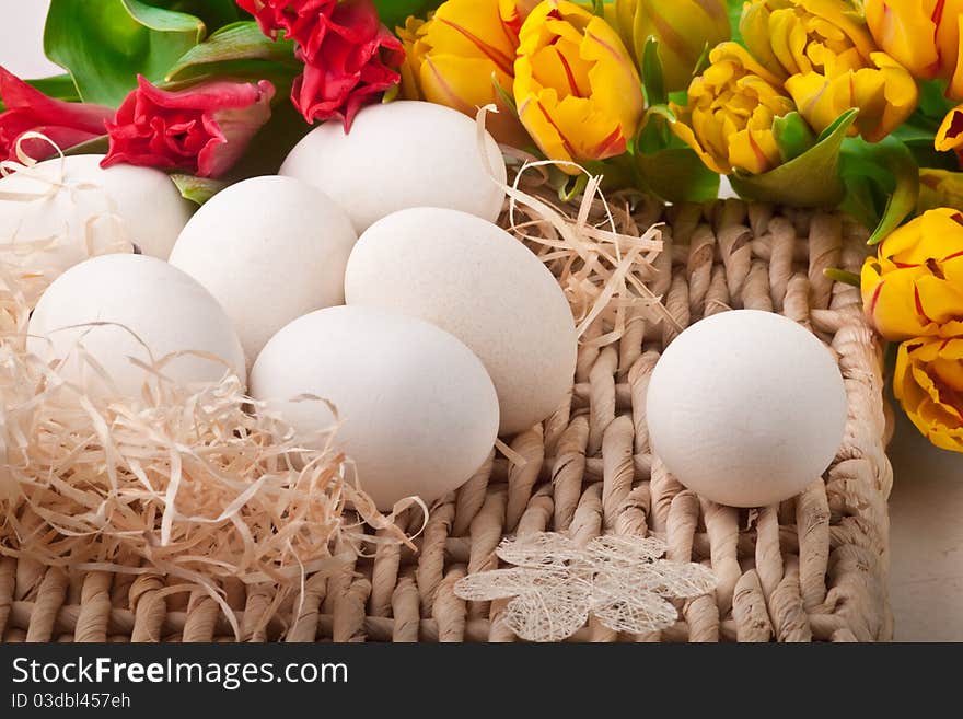 Seven white eggs and flowers lying on straw tray