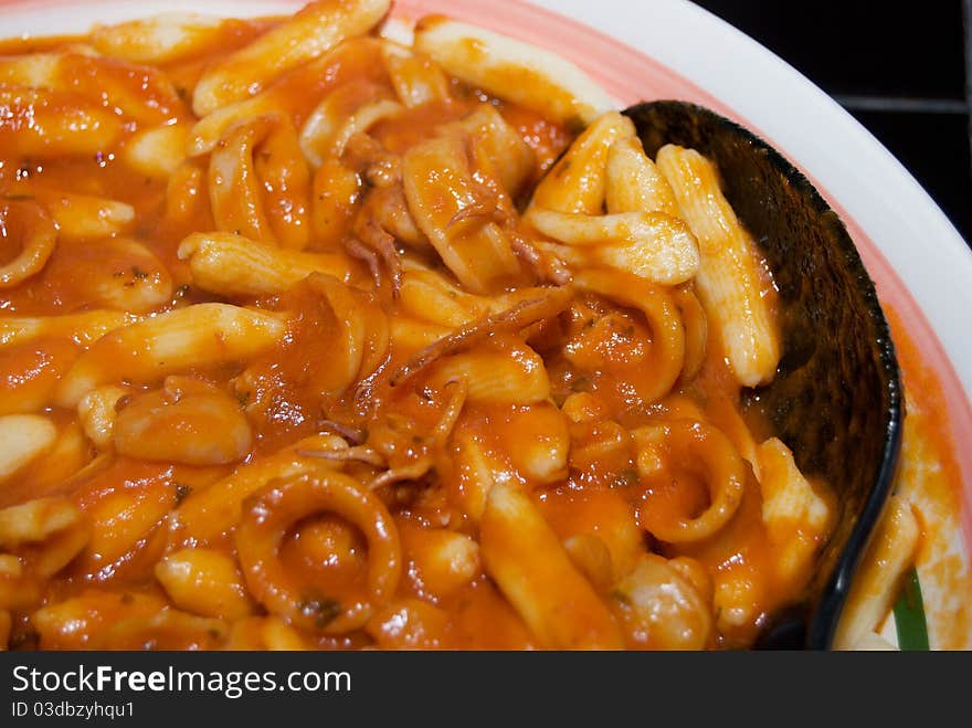 Cavatelli with an Italian Calamari Sauce in a serving dish on a black tile table. Cavatelli with an Italian Calamari Sauce in a serving dish on a black tile table.