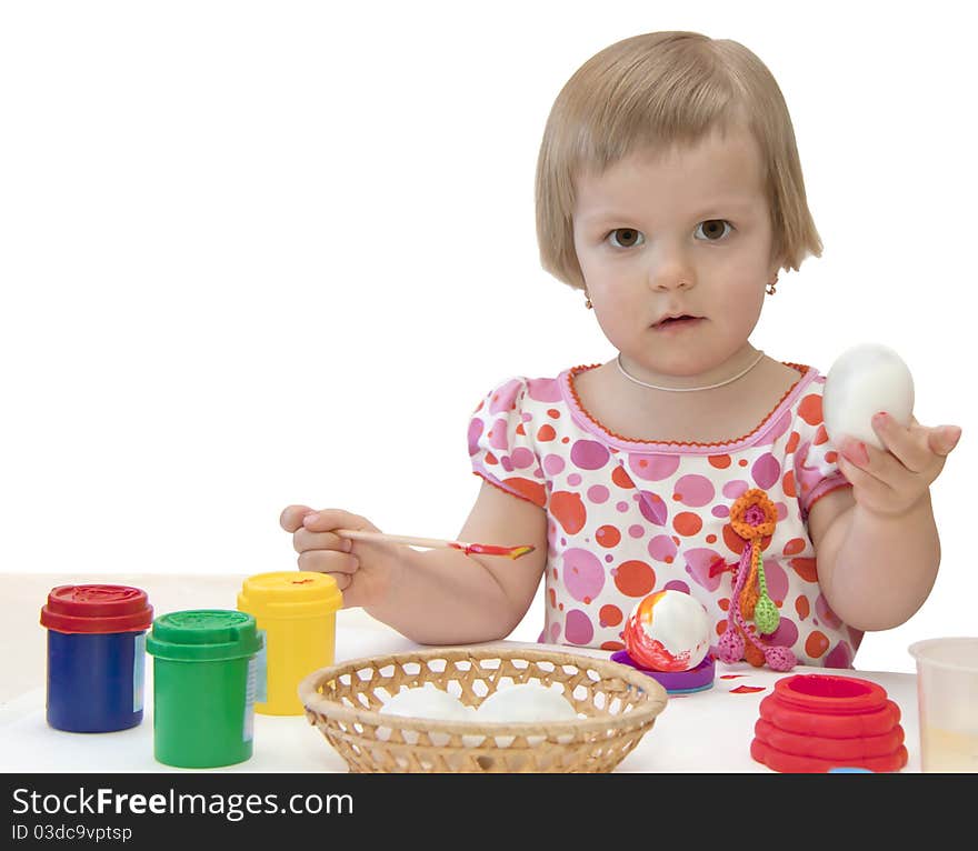 The girl decorates an egg and nearby there are paints. The girl decorates an egg and nearby there are paints