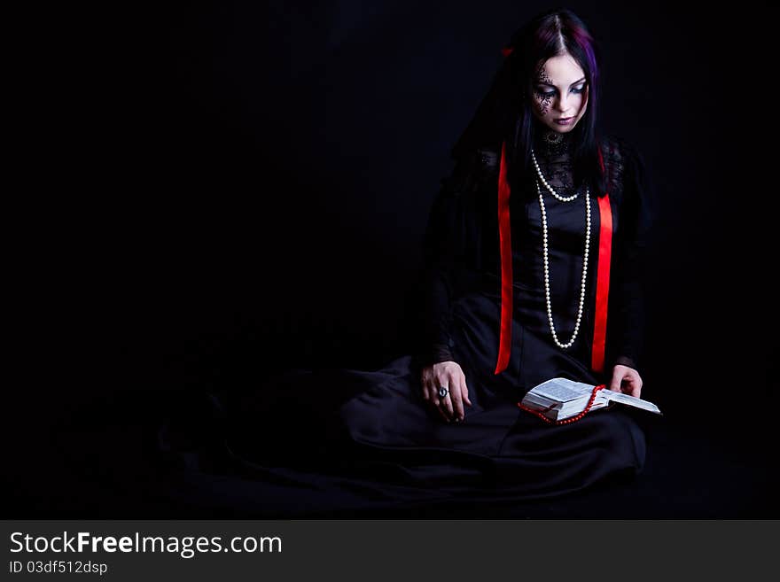 A goth-girl is reading the Bible. Isolated on black background