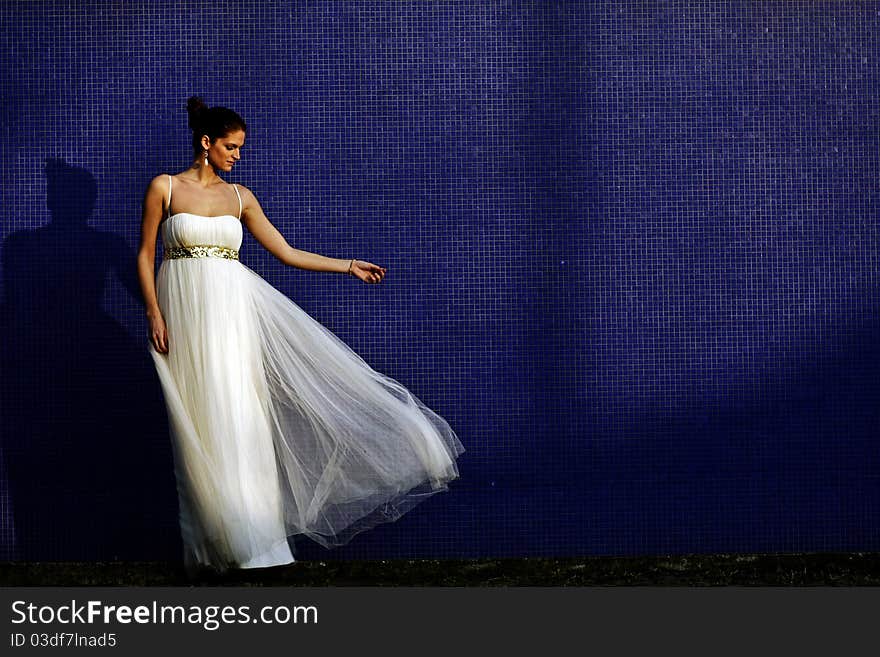 Beautiful brunet bride in wedding dress standing by the blue wall. Beautiful brunet bride in wedding dress standing by the blue wall