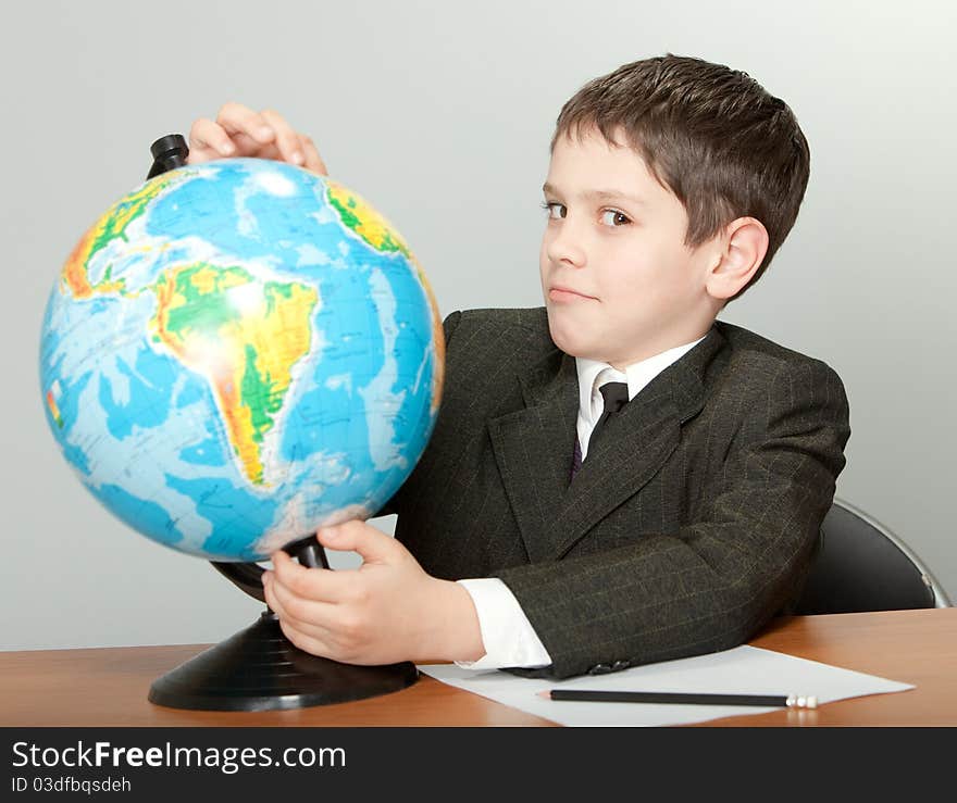 The schoolboy sits at a school desk and holds the globe