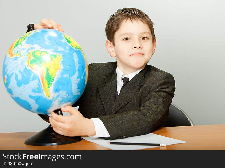 The schoolboy sits at a school desk and holds the globe