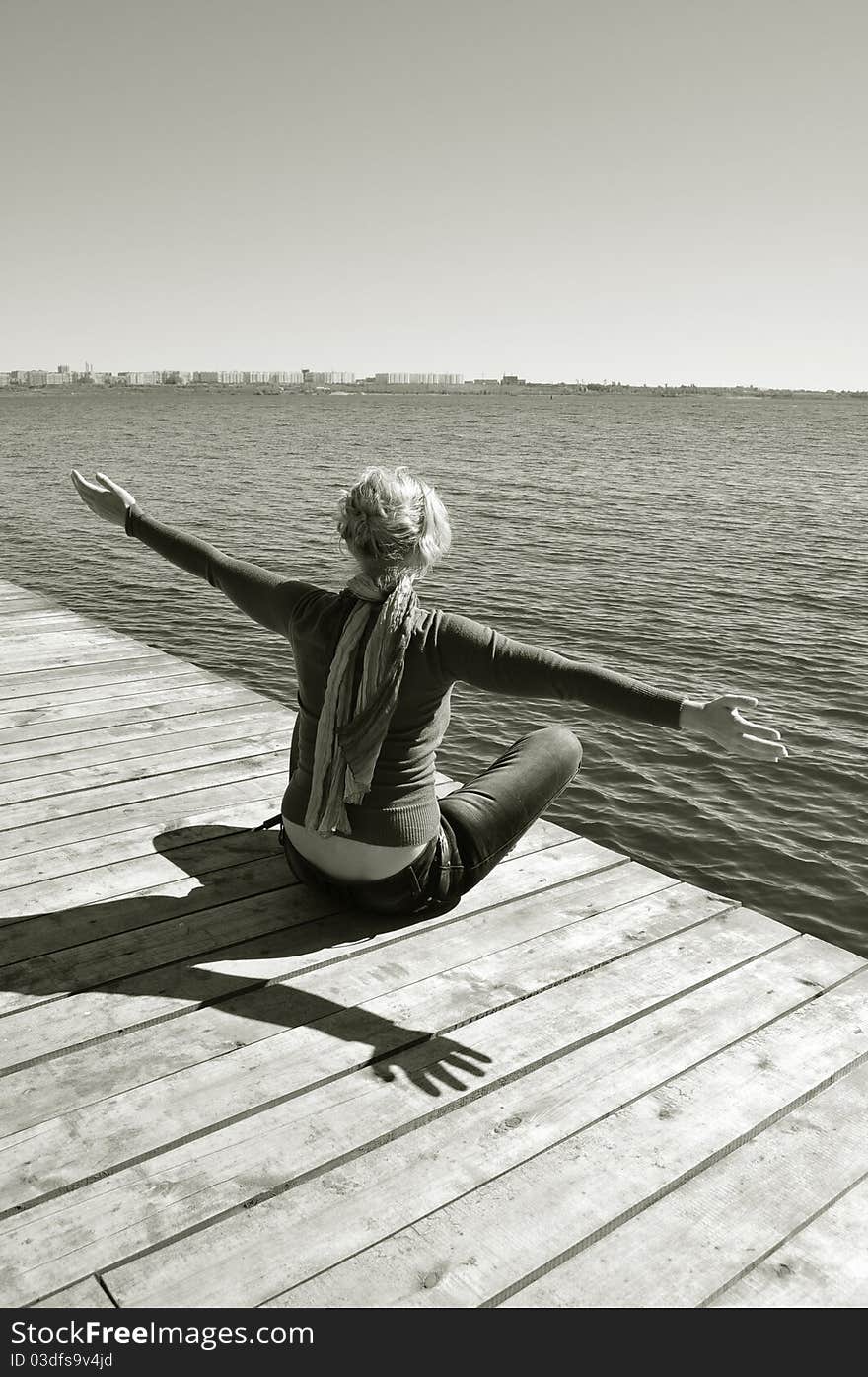 Happiness of freedom, healthy lifestyle, leisure and relax near the water, suburban rest, the woman reaches for the sunlight and breathe freshness of nature, she sits on the pier overlooking the blue water. Happiness of freedom, healthy lifestyle, leisure and relax near the water, suburban rest, the woman reaches for the sunlight and breathe freshness of nature, she sits on the pier overlooking the blue water