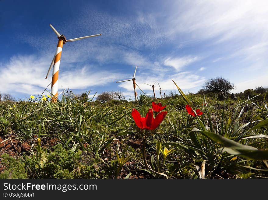 Orange wind turbine with red flowers and blue sky. Orange wind turbine with red flowers and blue sky