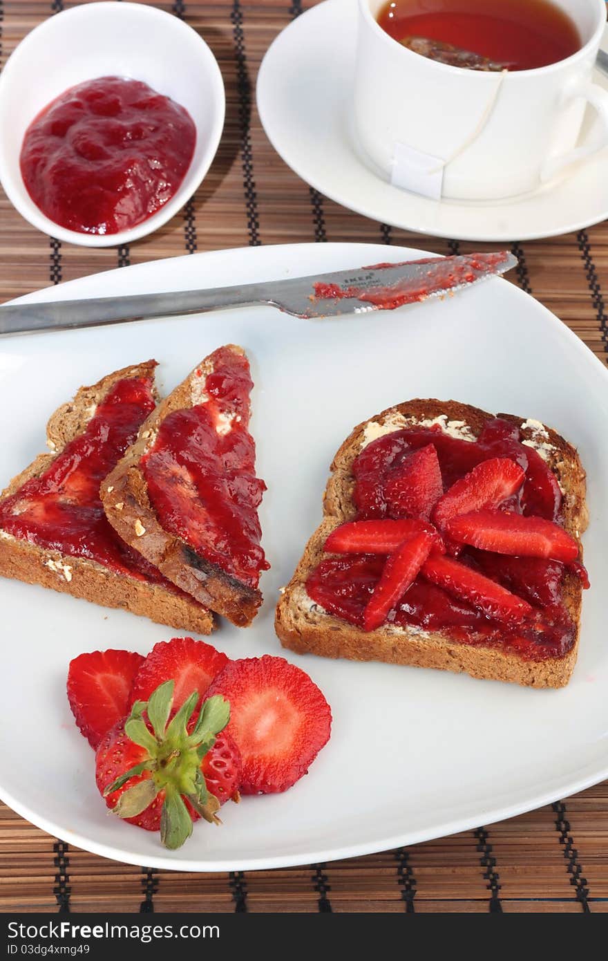 A simple but luxury breakfast of toast with strawberry jam and strawberries. Served with a cup of tea. A simple but luxury breakfast of toast with strawberry jam and strawberries. Served with a cup of tea.