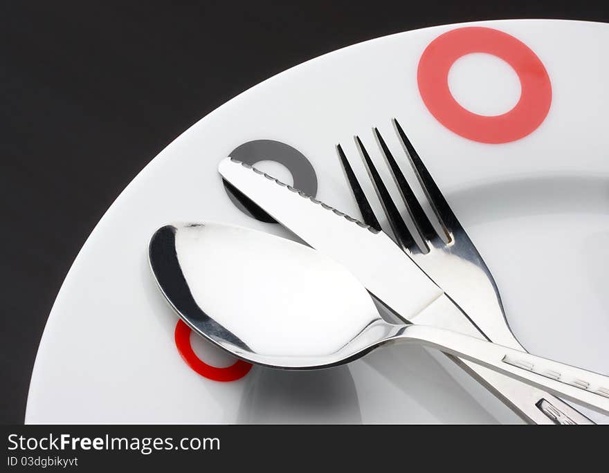 Place Setting: plate, spoon,fork and table knife on dark background. Place Setting: plate, spoon,fork and table knife on dark background