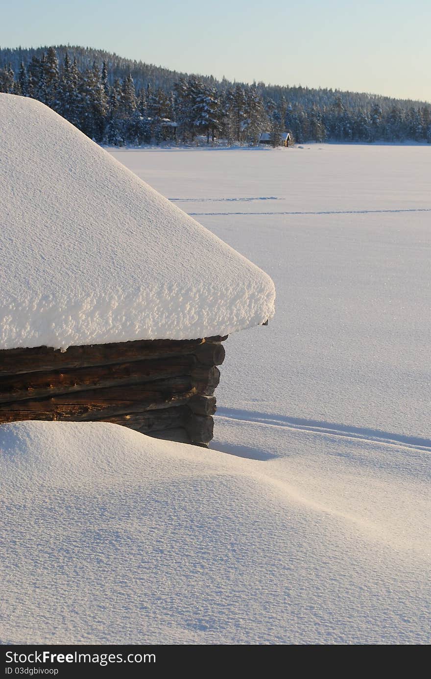 Two wooden small houses in the winter near to and it is far on the bank of the frozen lake. Two wooden small houses in the winter near to and it is far on the bank of the frozen lake.