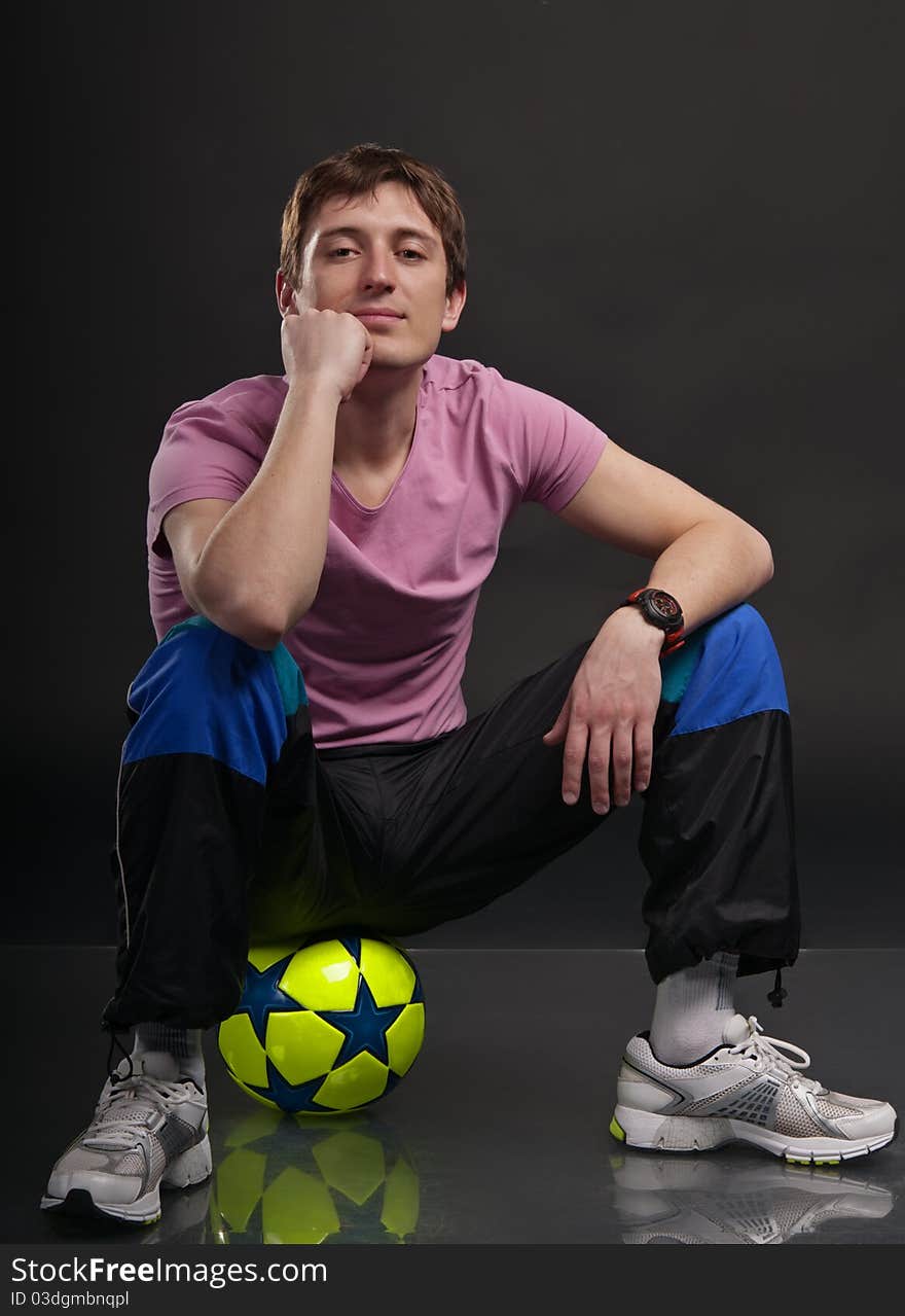 Man sits on a colorful soccer ball against a dark background