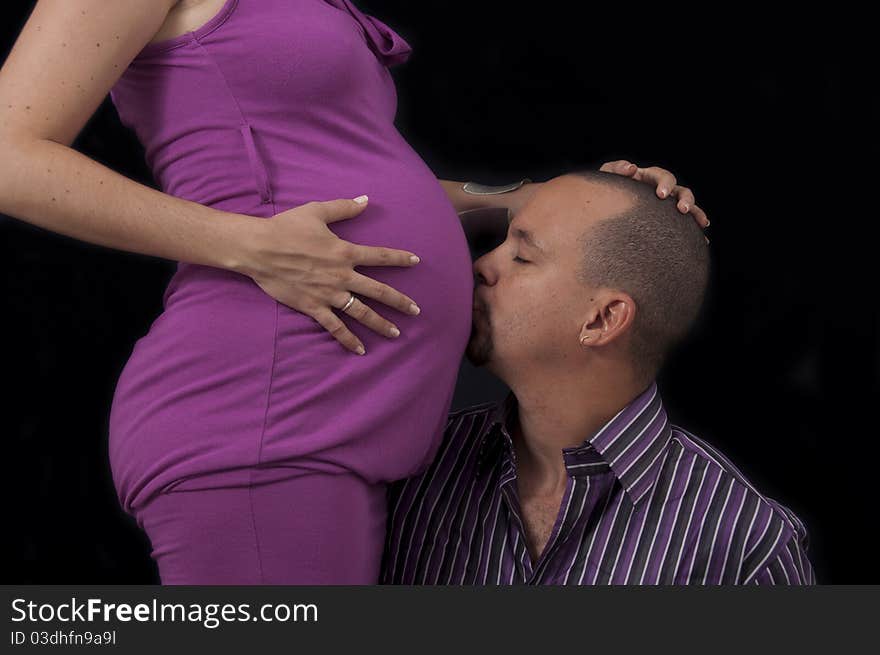 Portrait of young hispanic man kissing pregnant belly, isolated on black. Portrait of young hispanic man kissing pregnant belly, isolated on black