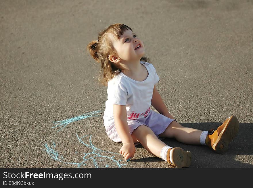 The child drawing a chalk on asphalt