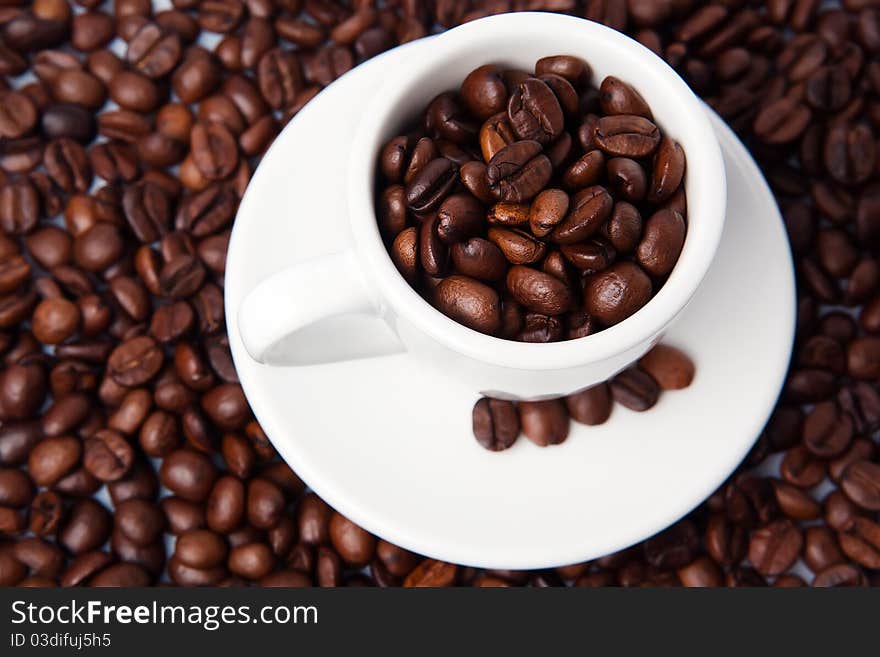 Closeup of small white espresso cup with plate, full of fresh brown roasted coffee beans. Closeup of small white espresso cup with plate, full of fresh brown roasted coffee beans