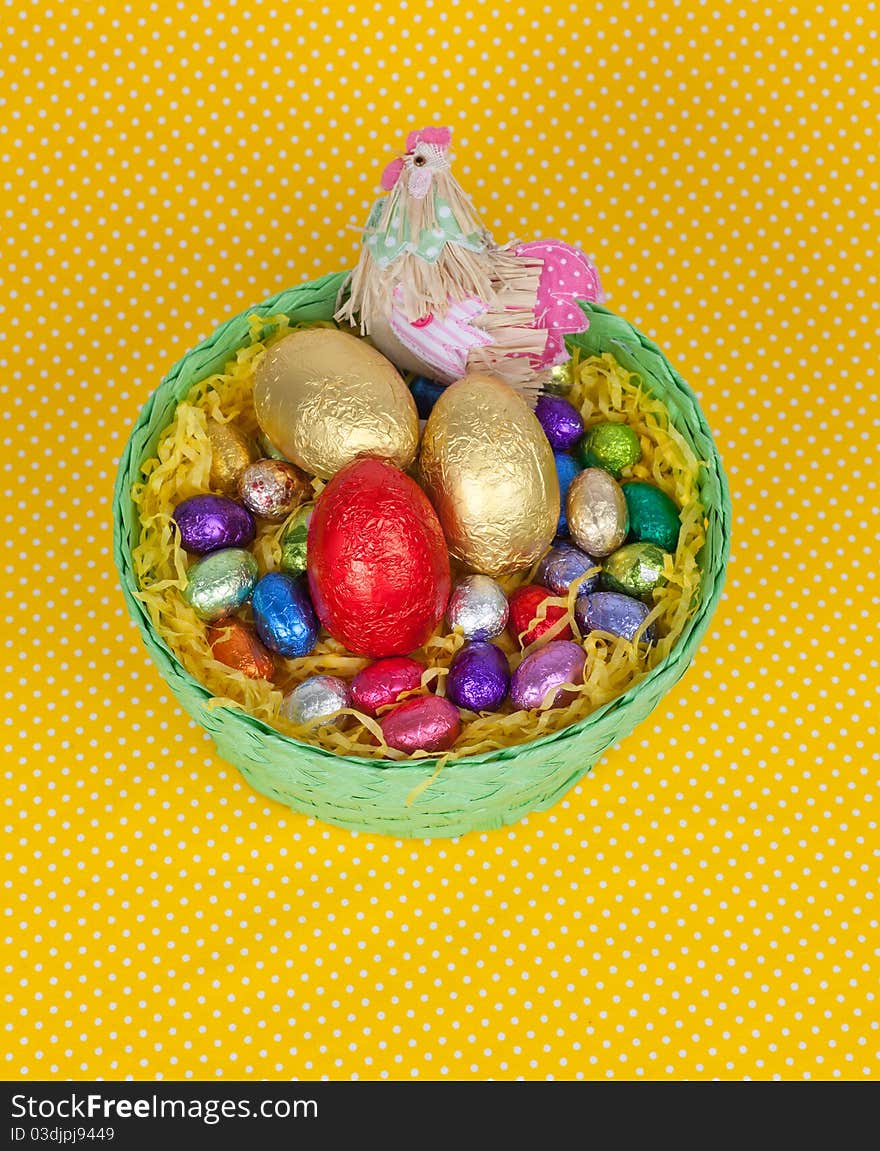 Colorful Easter chocolate eggs in a green basket isolated on a yellow background