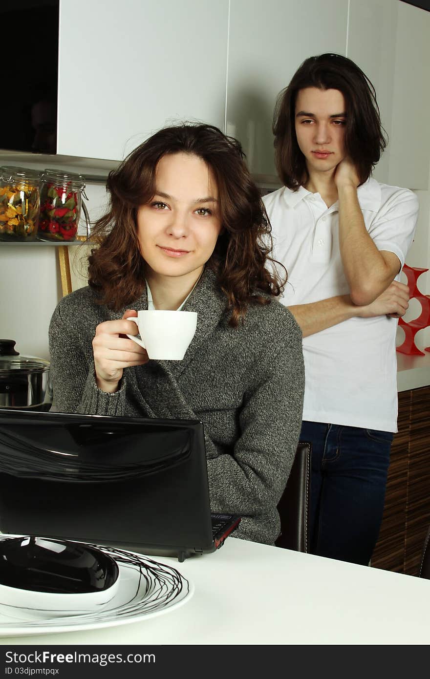 Young pair the woman and the man on kitchen in quarrel. The girl drinks coffee the guy behind her back is angry