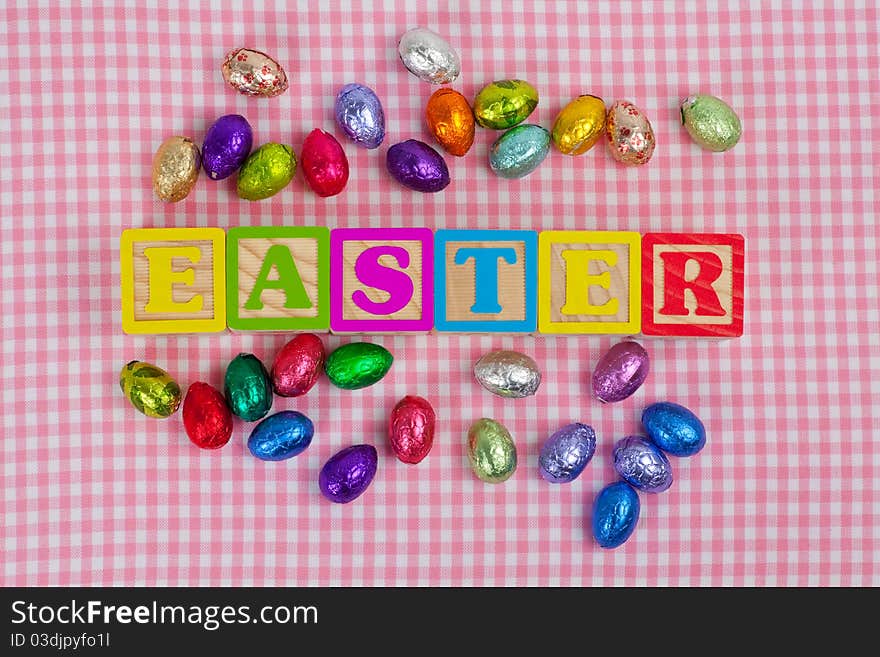 Easter word in wooden block letters with chocolate eggs isolated on a pink background