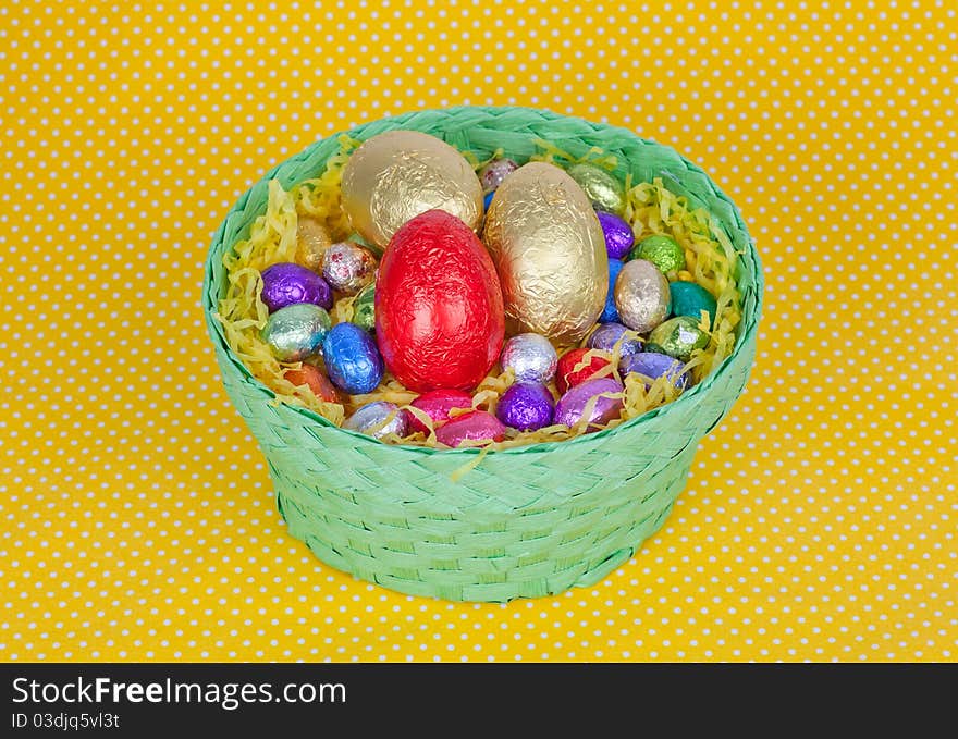 Colorful Easter chocolate eggs in a green basket isolated on a yellow background