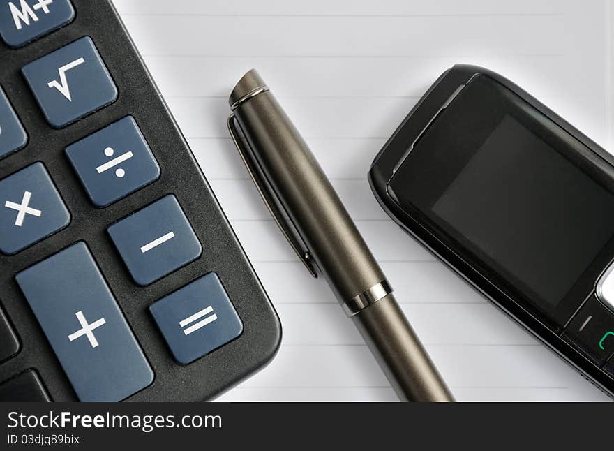 Pen, mobile phone and a calculator lying on a notebook