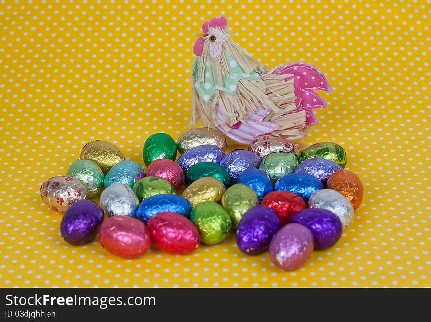 Chicken with Easter chocolate eggs on a yellow background