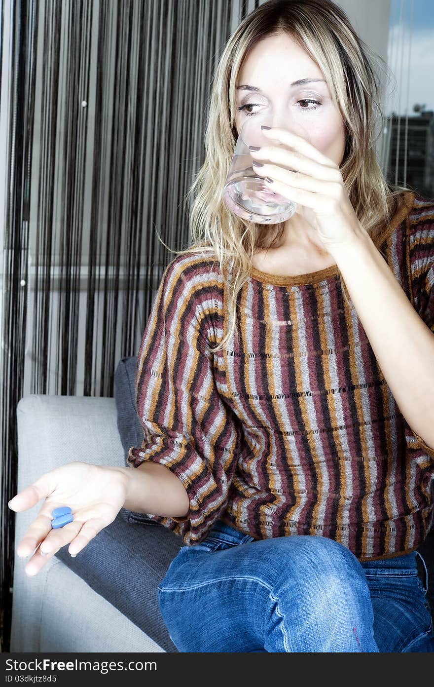 Blond woman taking a pill with a glass of water