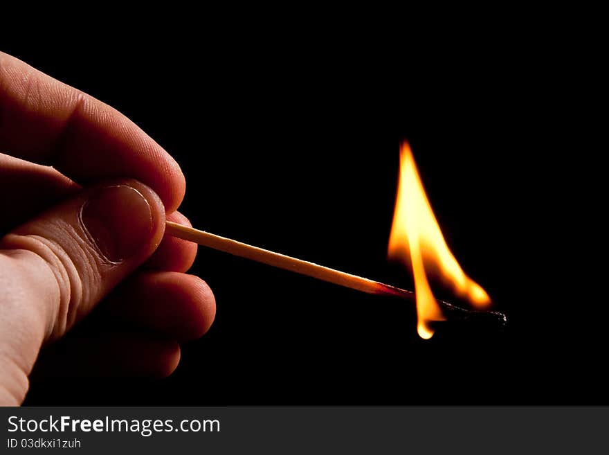 Hand holding fire match with smoke on black background