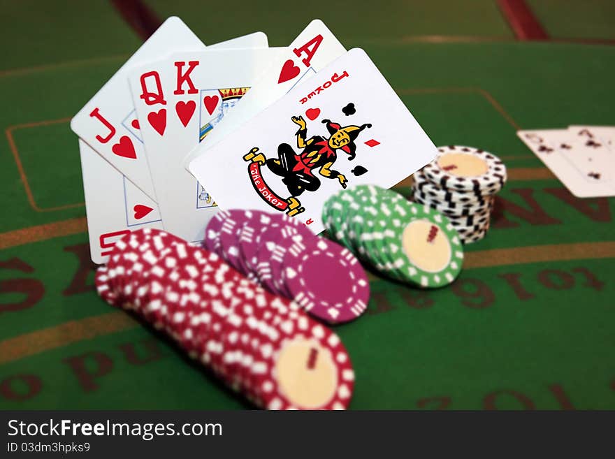 Green casino table with chips and a hand of a royal flush in a poker game and a joker in the pack