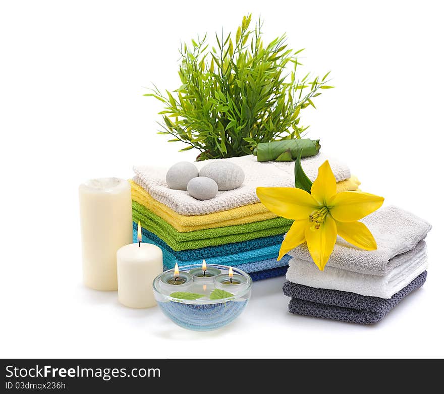 Stack of colorful towels with yellow lily and burn candles isolated on white background. Stack of colorful towels with yellow lily and burn candles isolated on white background