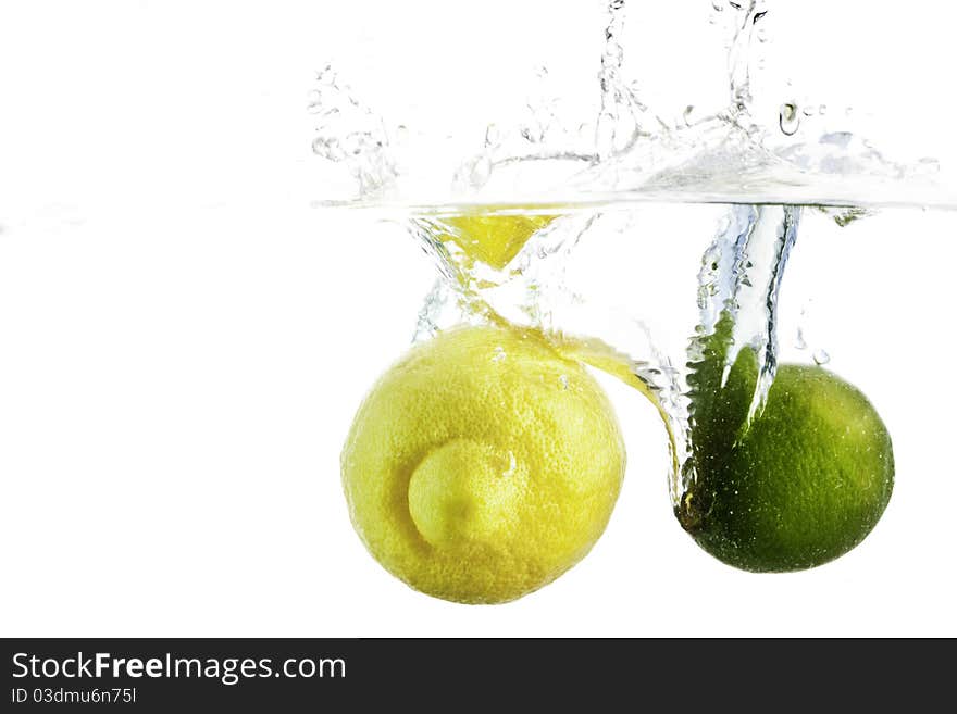 A lemon and a lime splashing into a clear vat of water isolated against a white background. A lemon and a lime splashing into a clear vat of water isolated against a white background