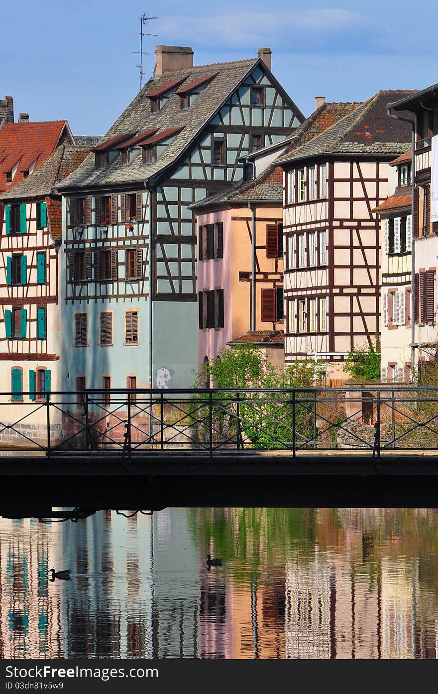 Traditional half-timbered houses in Strasbourg Alsace France reflecting in Ille River banks with footbridge in foreground. Traditional half-timbered houses in Strasbourg Alsace France reflecting in Ille River banks with footbridge in foreground.