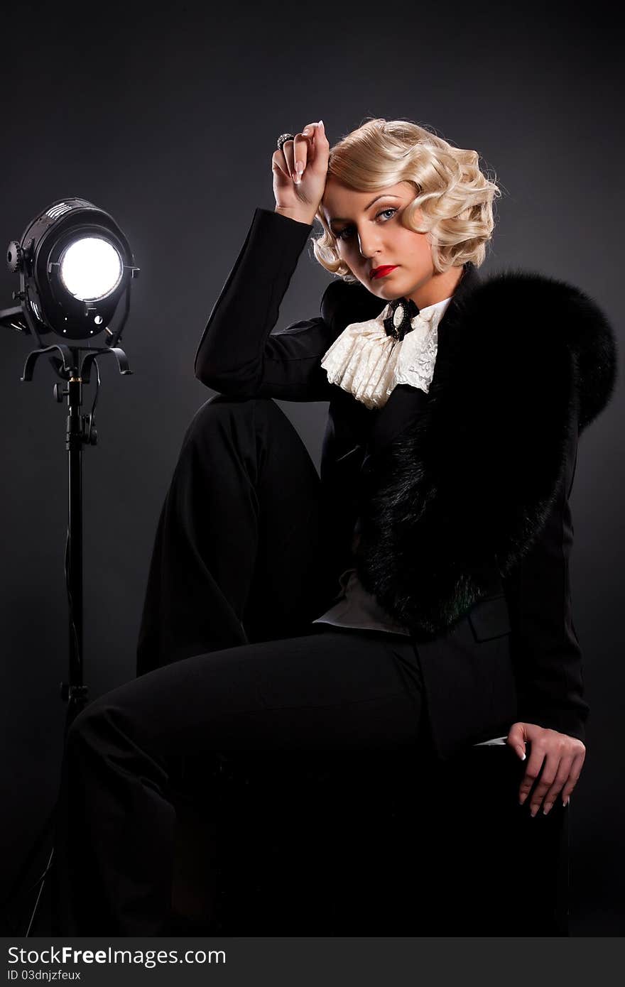 Young blonde woman dressed in retro style sitting near the studio lighting. Young blonde woman dressed in retro style sitting near the studio lighting