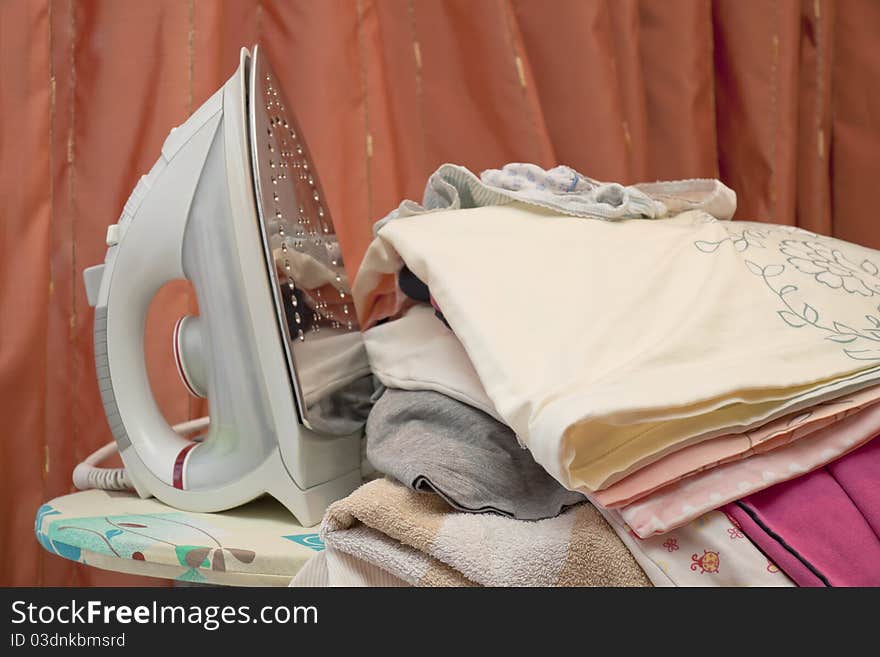 Iron on an ironing table near a heap of the washed linen