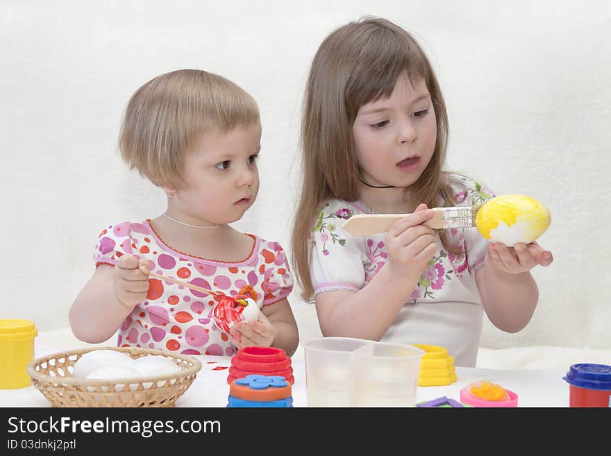 Children with enthusiasm paint Easter eggs on the white. Children with enthusiasm paint Easter eggs on the white