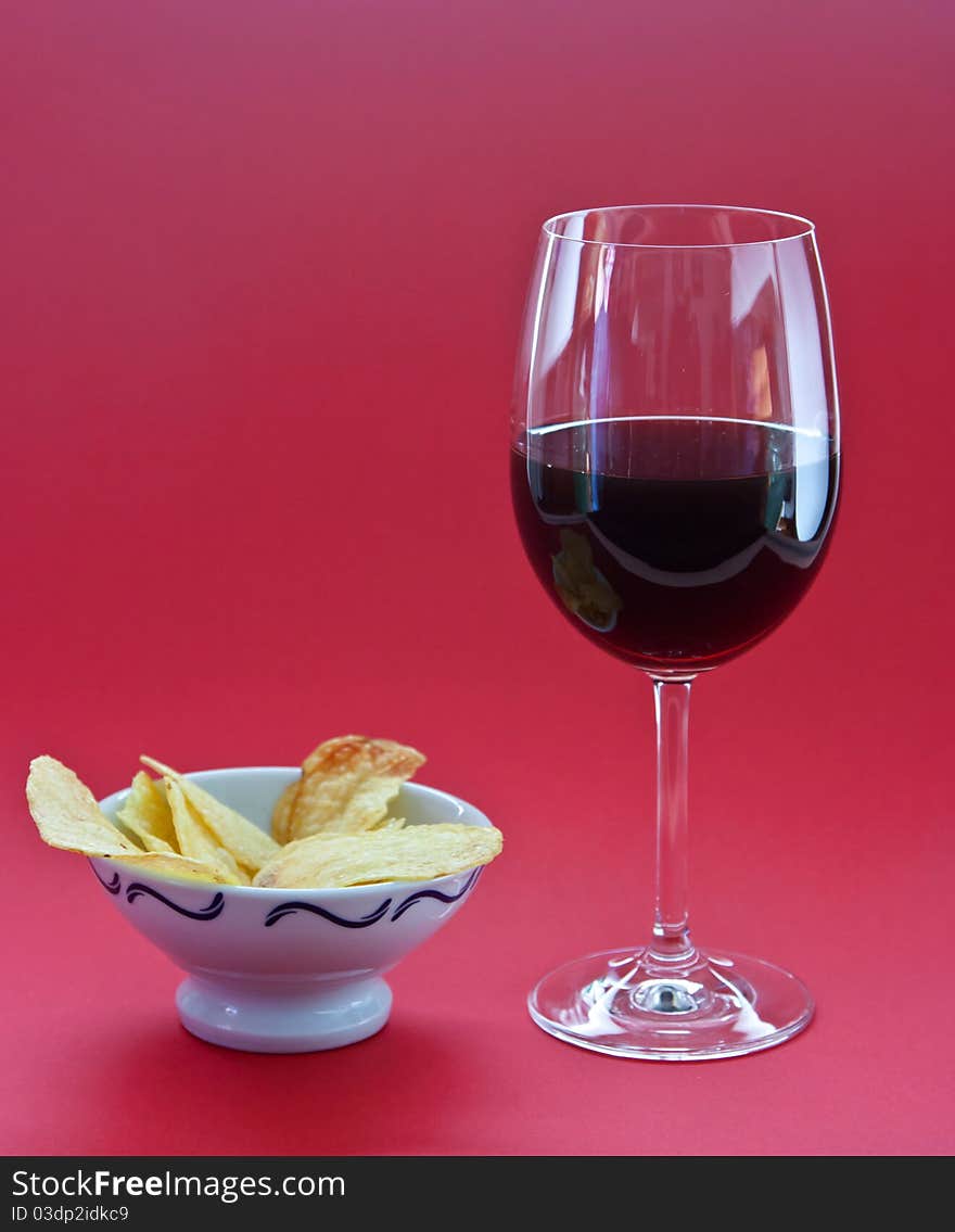 A glass of wine and chips on red background