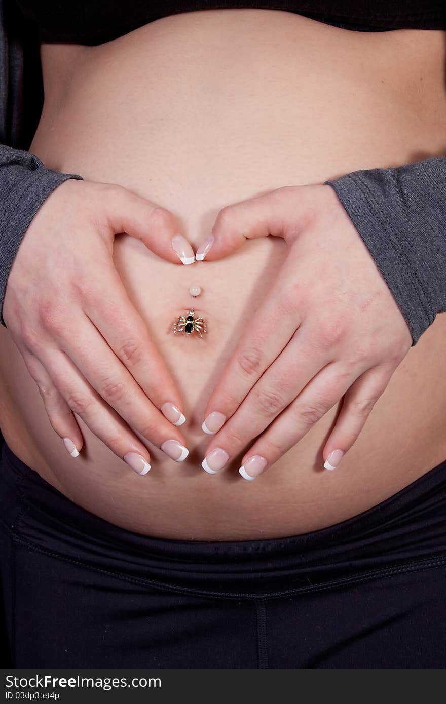 Close up of a womans hands in shape of heart over pregnant belly button. Close up of a womans hands in shape of heart over pregnant belly button