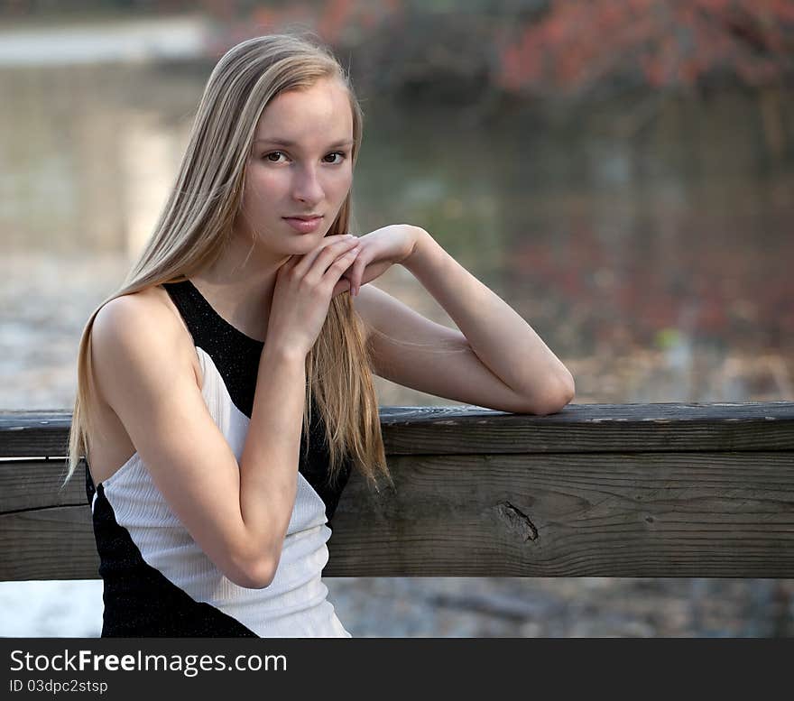 A lovely portrait of a pretty blond teenager in a natural setting and using natural light, by a lake with foliage visible in the background. A lovely portrait of a pretty blond teenager in a natural setting and using natural light, by a lake with foliage visible in the background.