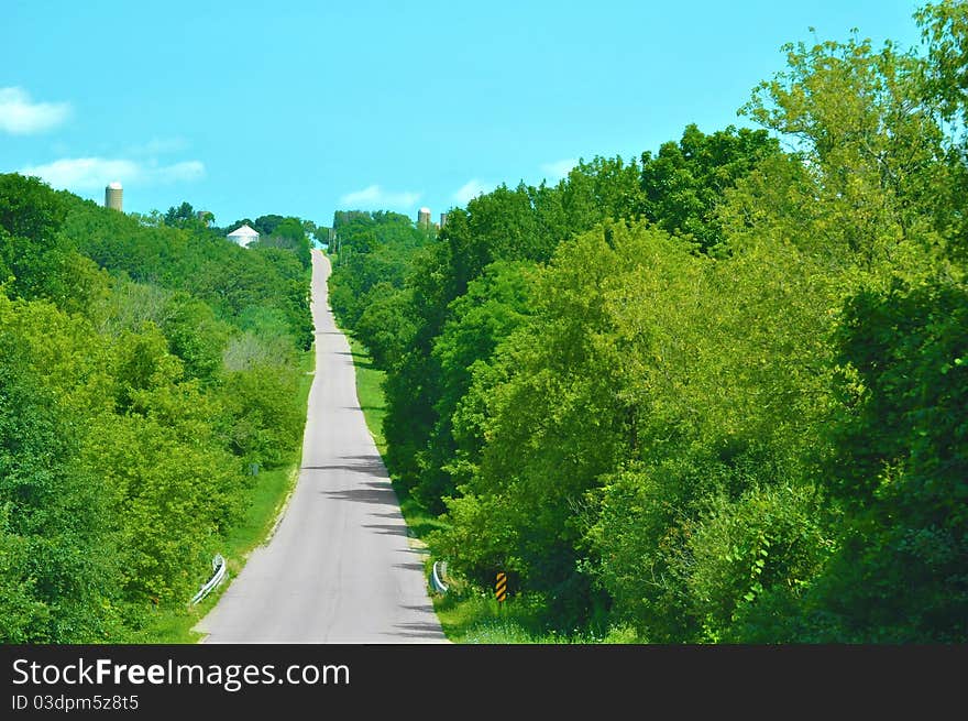 A paved country road through green trees and below an aqua sky. A paved country road through green trees and below an aqua sky