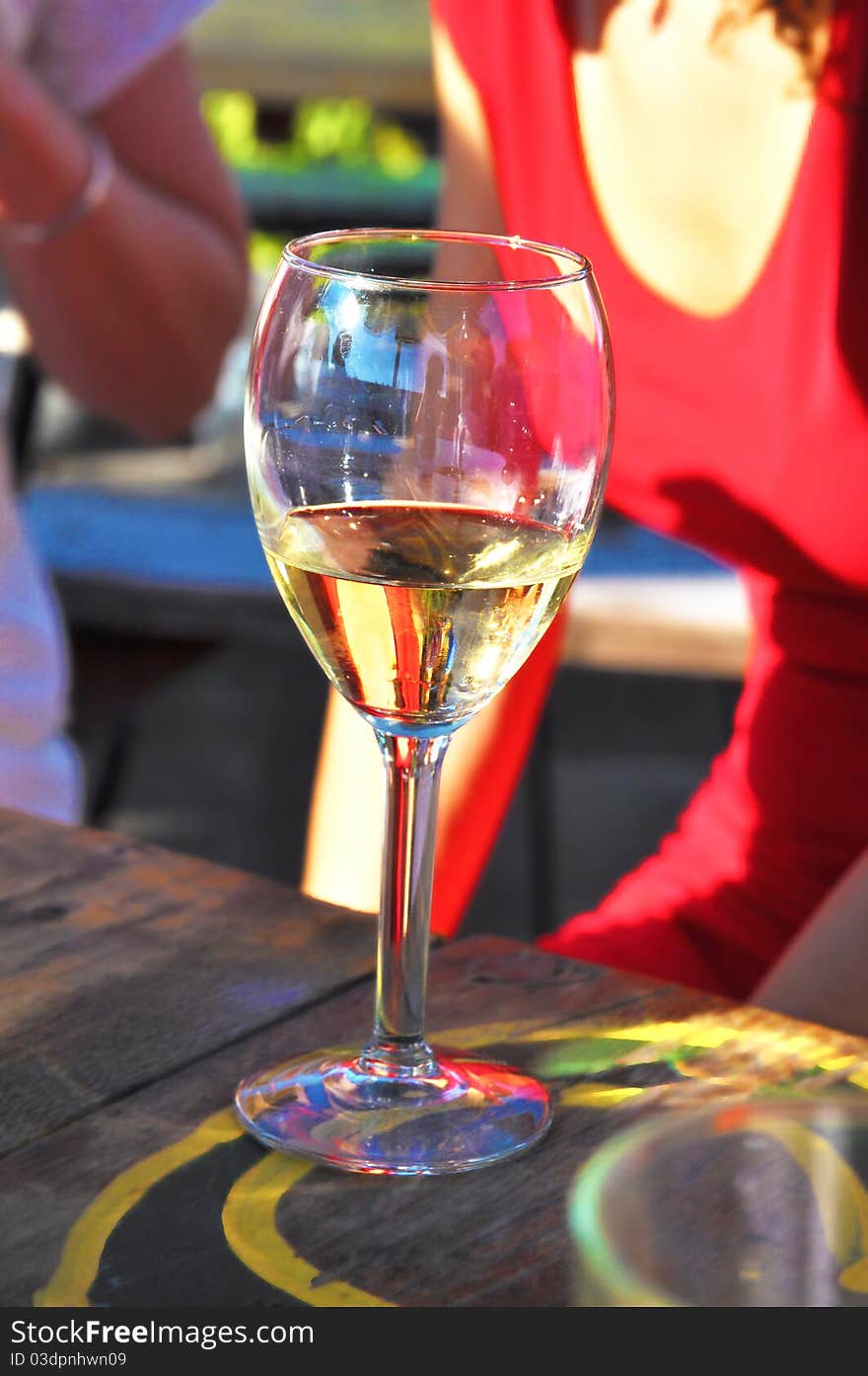 A glass of white wine sitting on a table with dressed up women in the background. A glass of white wine sitting on a table with dressed up women in the background