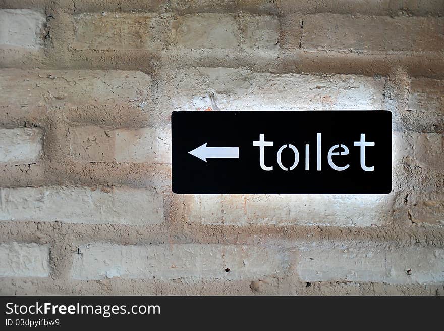 Fluorescent toilet sign in black on brique rouge wall.