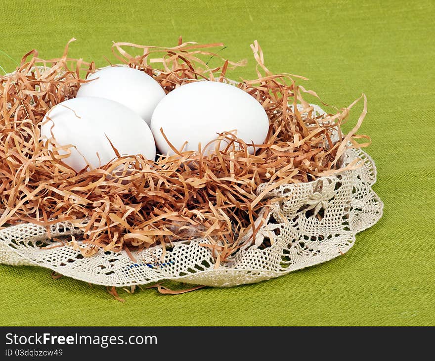 Easter composition: nest with three white eggs on green flax background with lace decoration