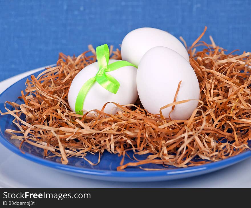 Easter composition: nest with three white eggs on blue plate